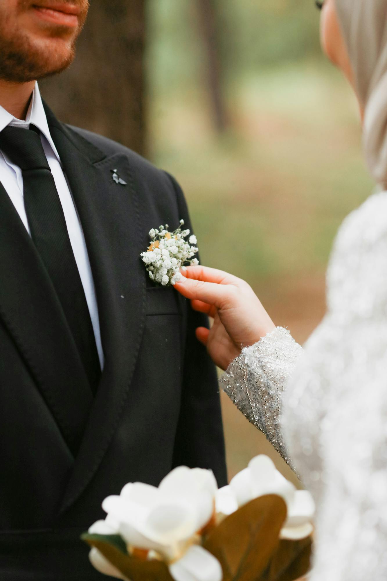 A close-up of a bride adjusting a groom's boutonniere during an outdoor wedding ceremony.